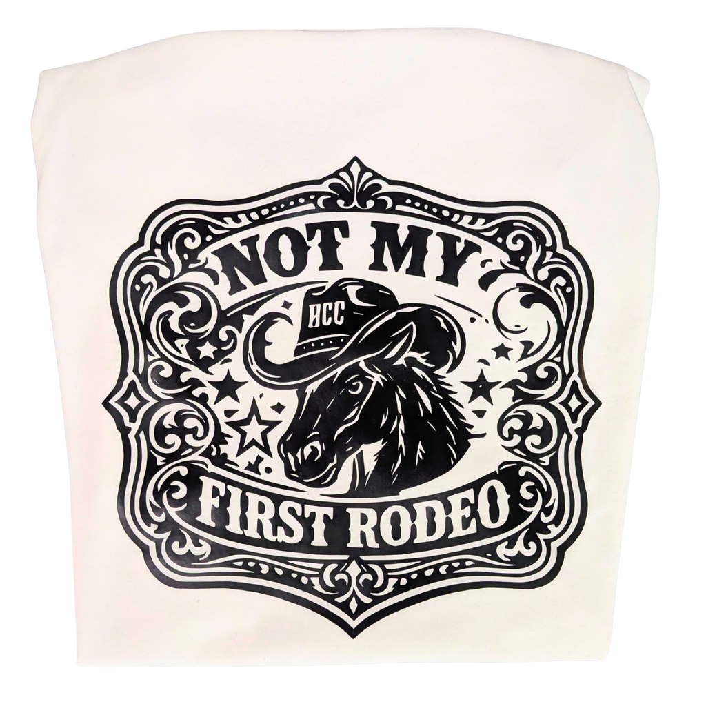 An off-white fabric item, likely a tote bag or pouch, featuring a black western-themed graphic print with a horse illustration and the text 'NOT MY FIRST RODEO' and 'HCC'.