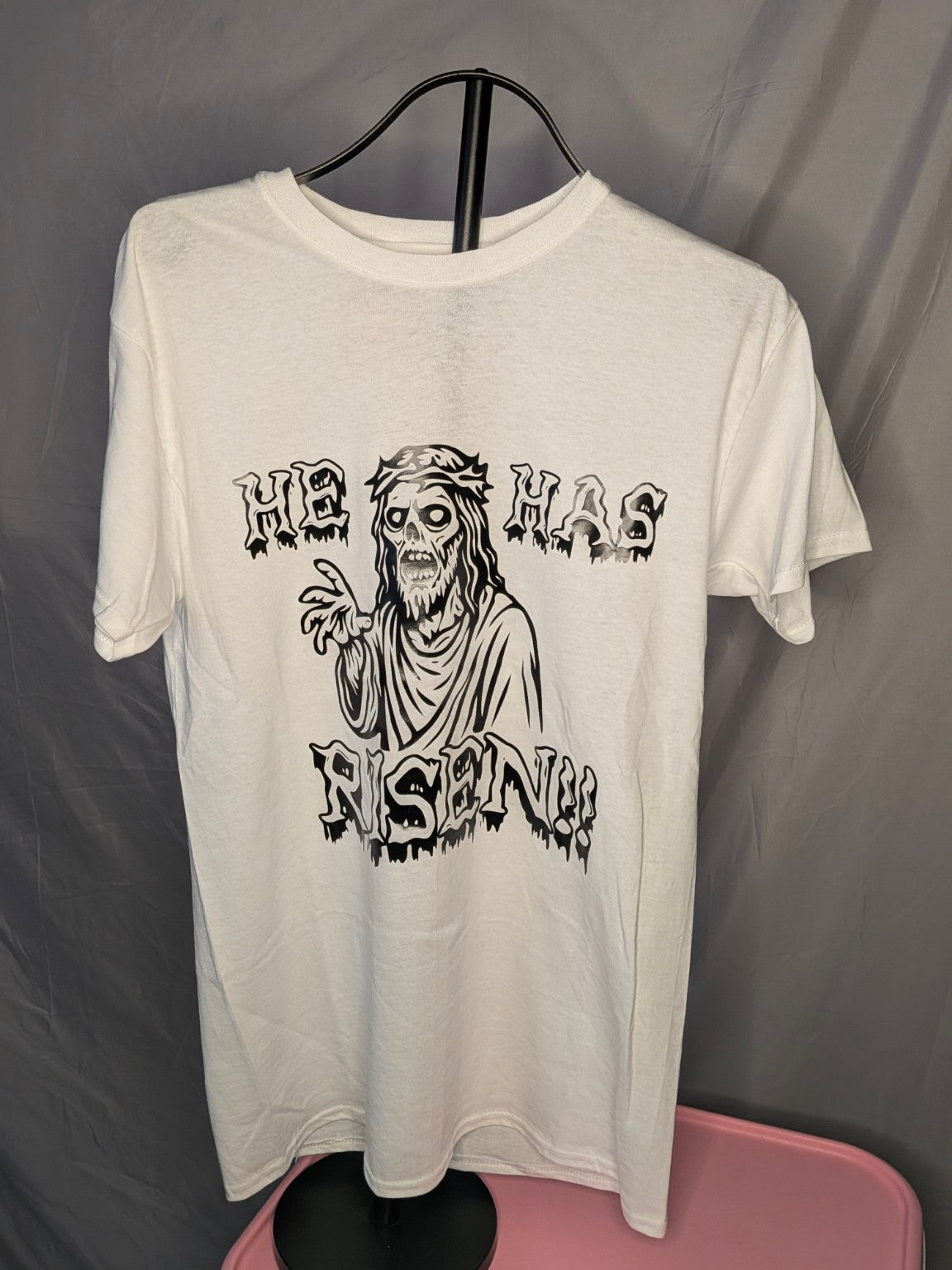 He Has Risen graphic T-shirt in white with zombie Jesus graphic on gray backdrop